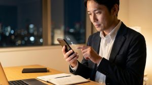夜、自宅のデスクで、副業用スマートフォンのセキュリティ設定を慎重に調整する日本の会社員男性。